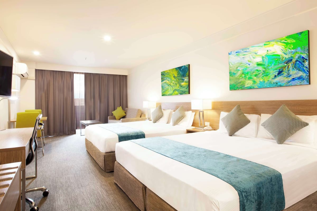 A hotel room with two beds, a desk, a chair, and a TV.