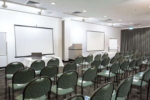 A conference room with rows of chairs, a projector screen, a laptop on a table, and a whiteboard.