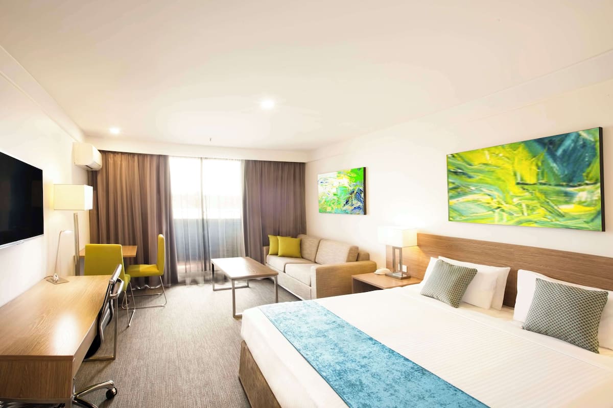 A hotel room with a large bed, a desk, a sofa, and a TV.