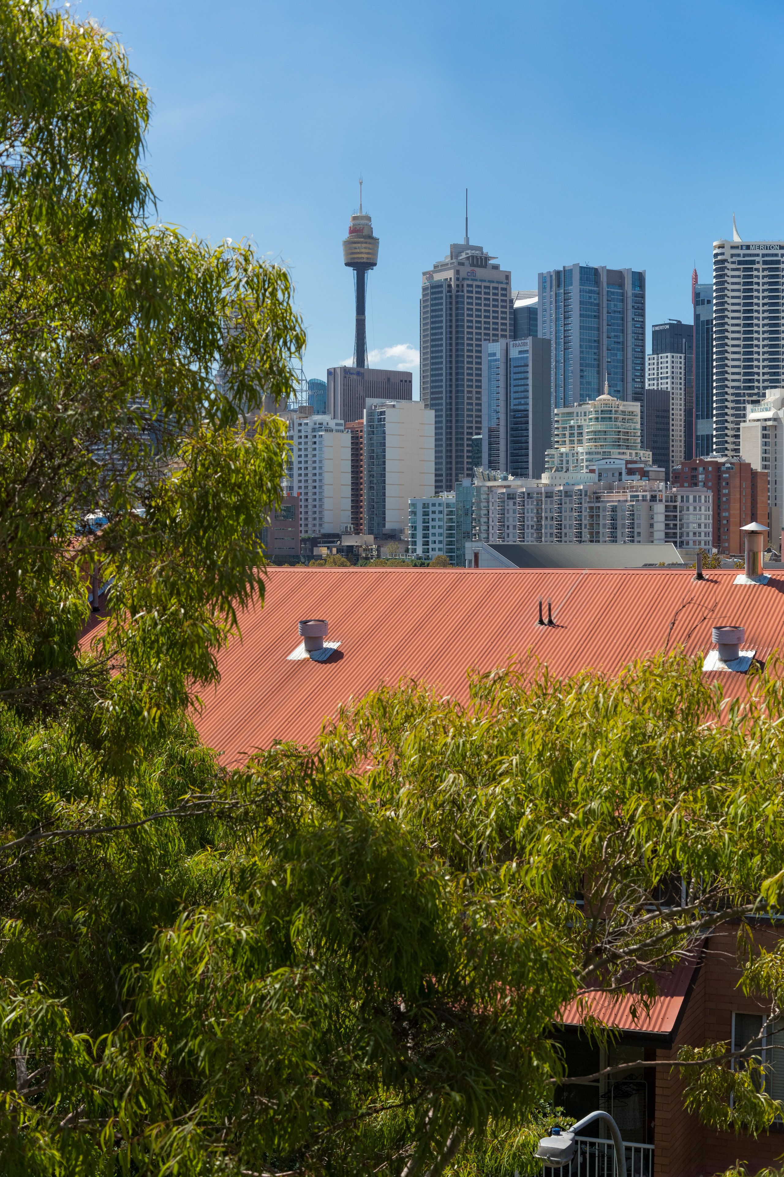 A city skyline with modern high-rise buildings, a prominent tower, and a red-roofed building in the foreground.
