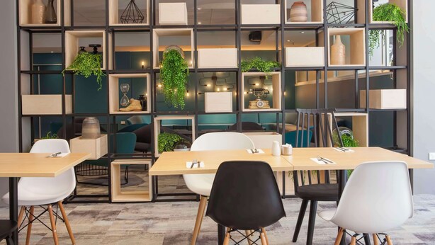 A modern dining area with a wooden table and chairs, a black and white color scheme, and a decorative wall with shelves and plants. - Metro Aspire Hotel, Sydney (Ultimo)