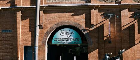 Een gebouw van baksteen met een bord voor Paddy's Markets, inclusief openingstijden en website.