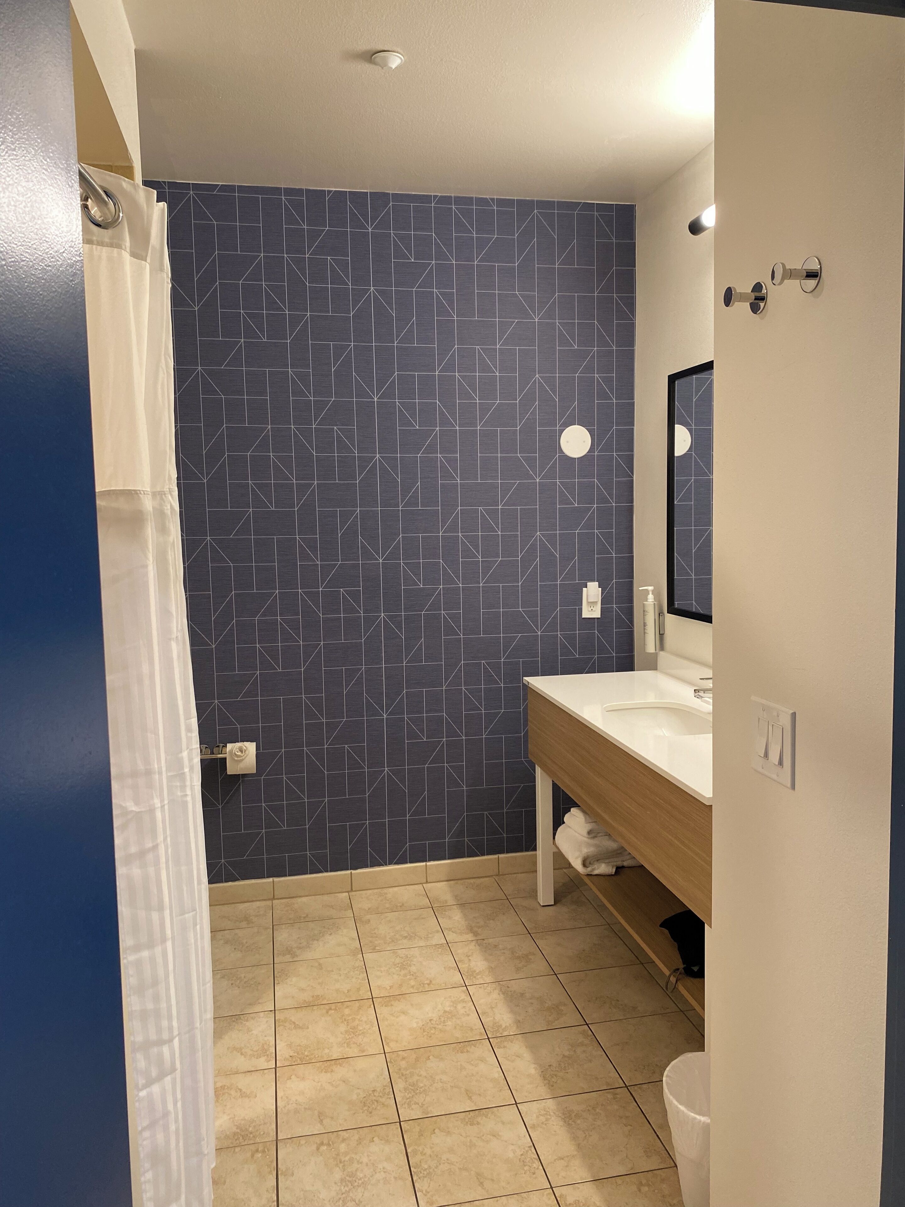 Een badkamer met een wand met een geometrisch patroon, een witte wastafel, een spiegel en een douchegordijn.