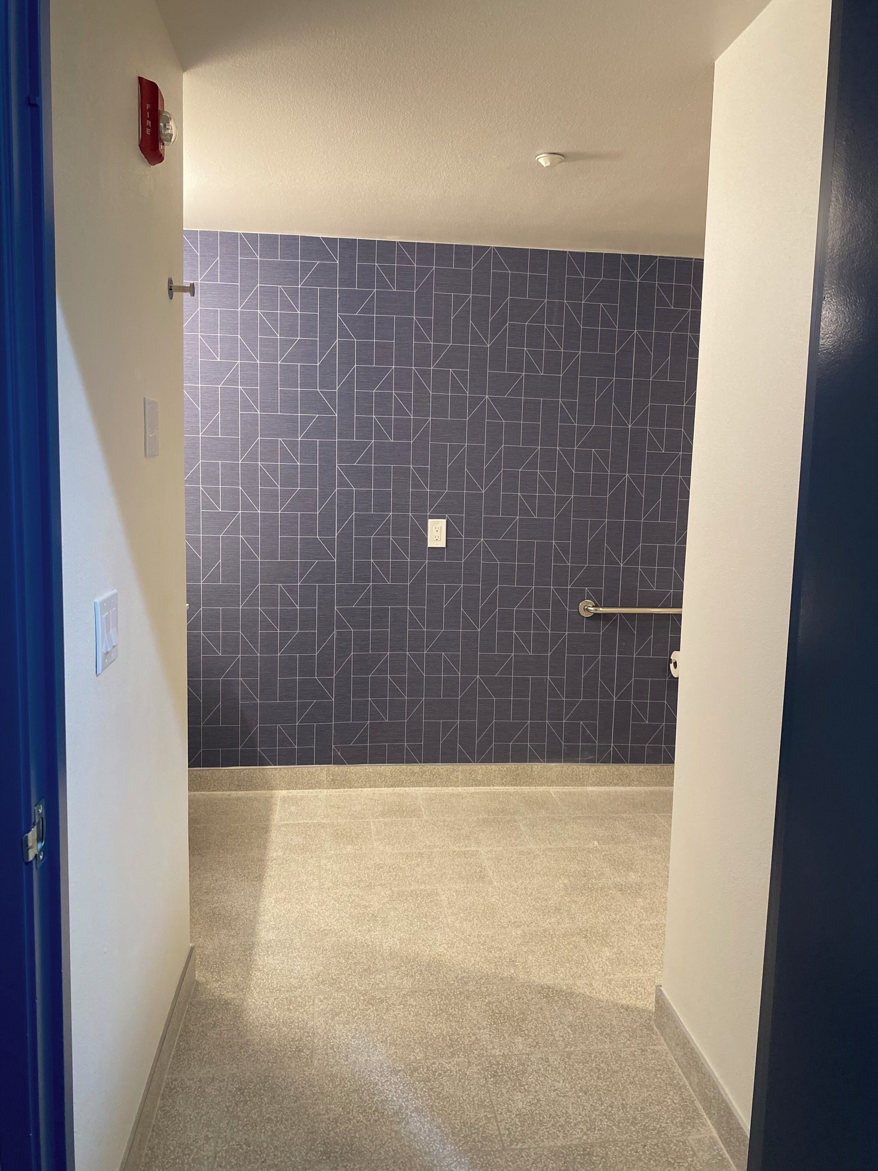 A hallway with a geometric patterned wall, a door with a horizontal bar, and a blue door frame.