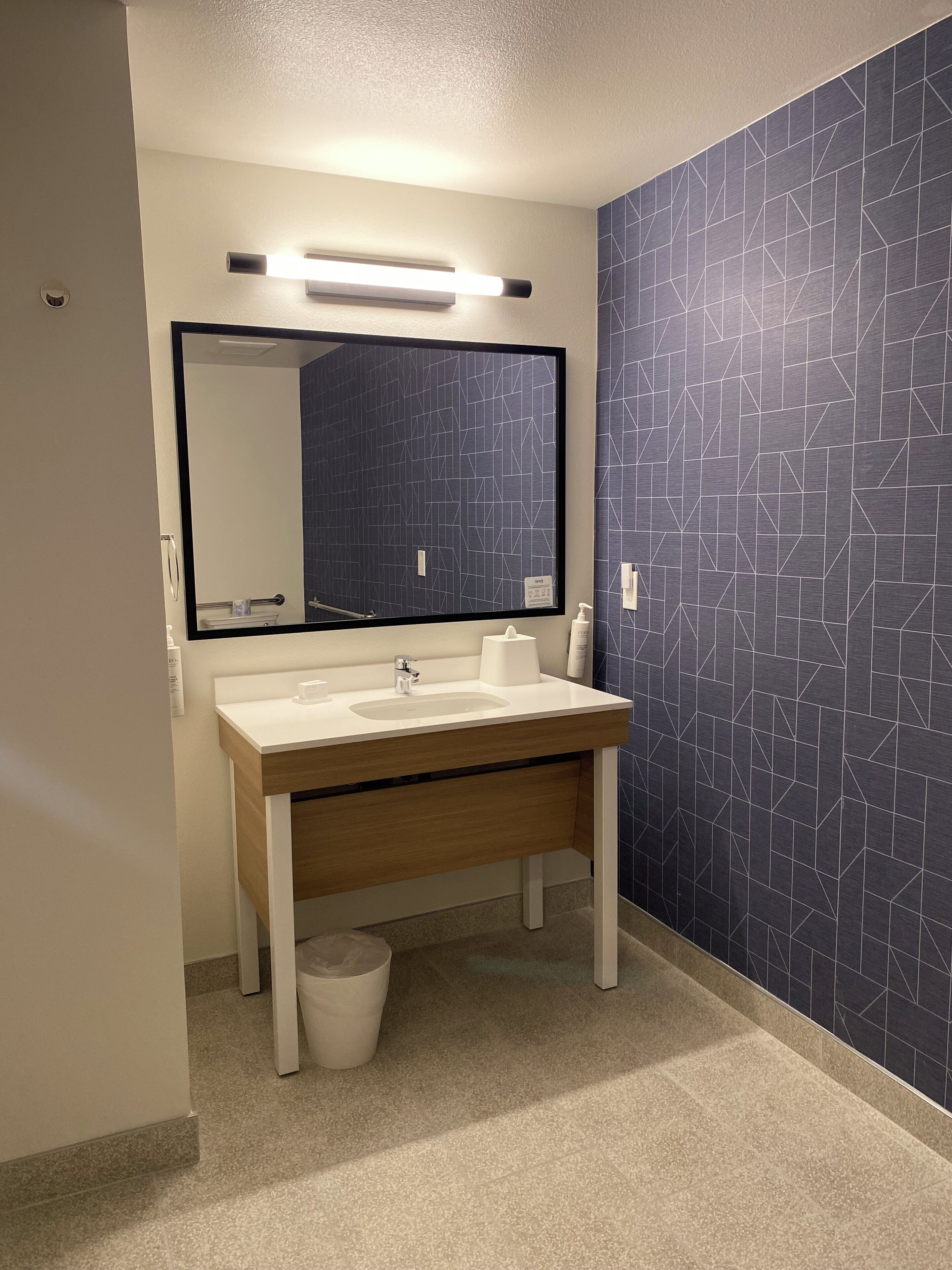 A modern bathroom with a white sink, a large mirror, and a blue geometric-patterned wall.