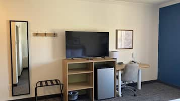 Ett hotellrum med en platt-TV, ett skrivbord med en dator, en stol, ett litet kylskåp, en papperskorg och en spegel.