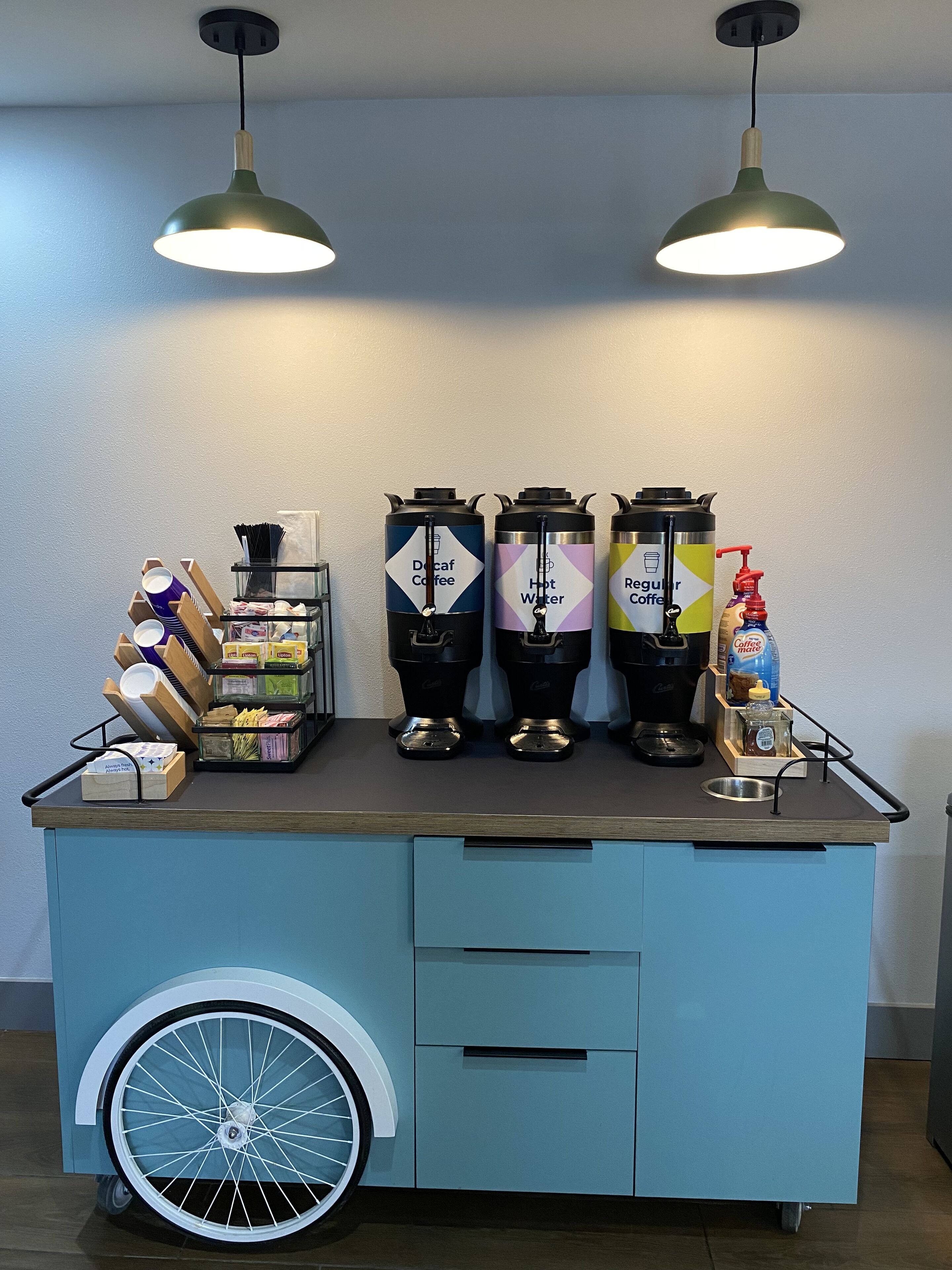 A coffee station with dispensers for decaf coffee, hot water, and regular coffee, along with a bottle of coffee mate and a coffee machine.