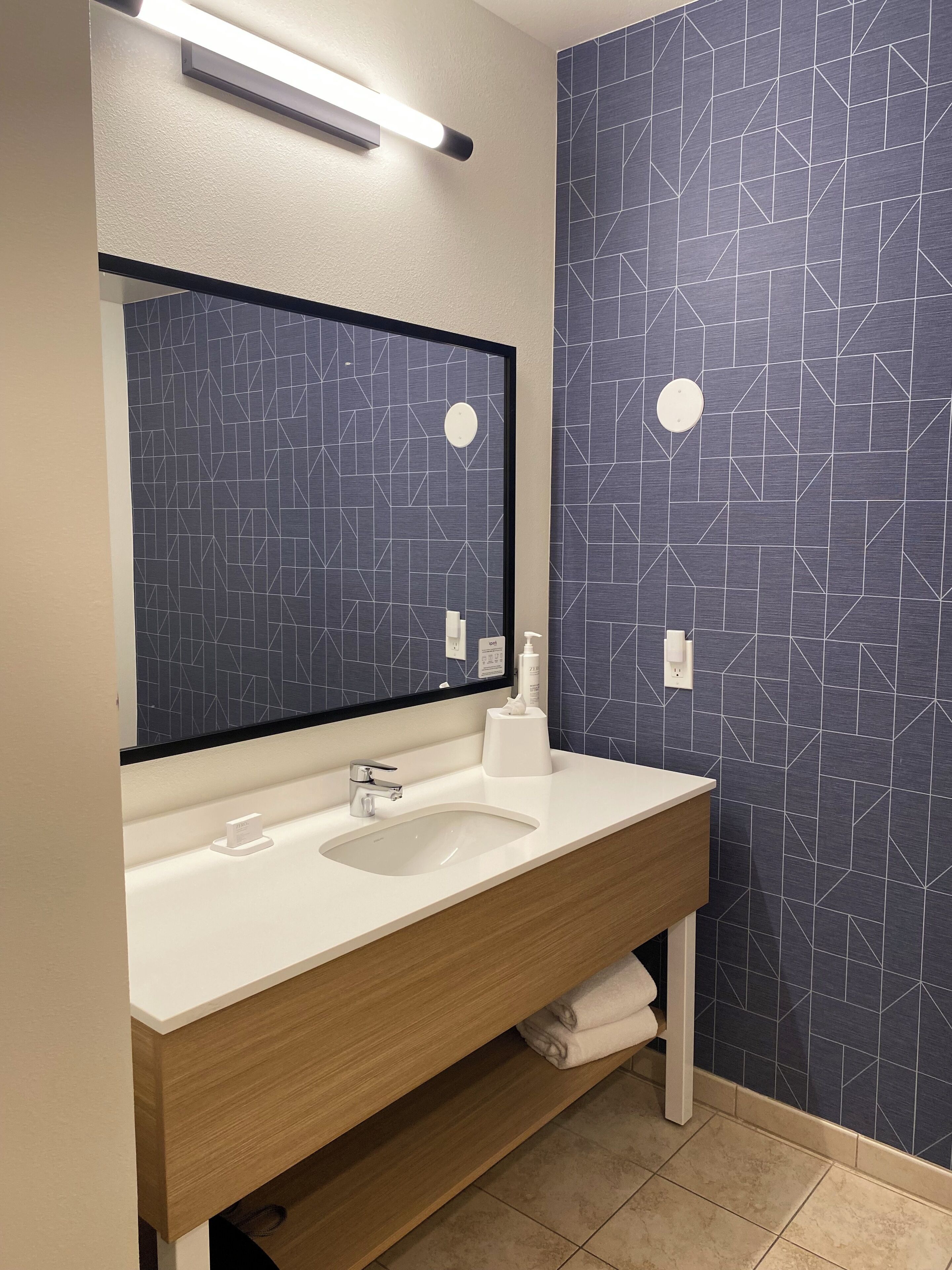 Ein modernes Badezimmer mit einem weißen Waschbecken, einem Spiegel und einer Wand mit geometrischem Muster.