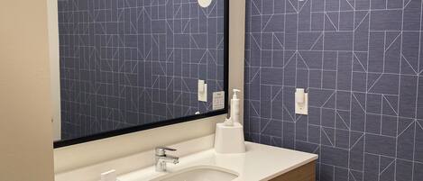Ein modernes Badezimmer mit einem weißen Waschbecken, einem Spiegel und einer Wand mit geometrischem Muster.