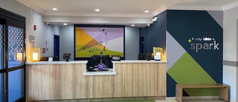 Un espace d’accueil d’hôtel au design moderne, comprenant un comptoir d’accueil, un grand tableau abstrait et un panneau indiquant « Hilton Honors ».
