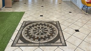 A hotel lobby with a tiled floor, a green area rug, a seating area with a bench, and a television screen displaying 'Trending'.