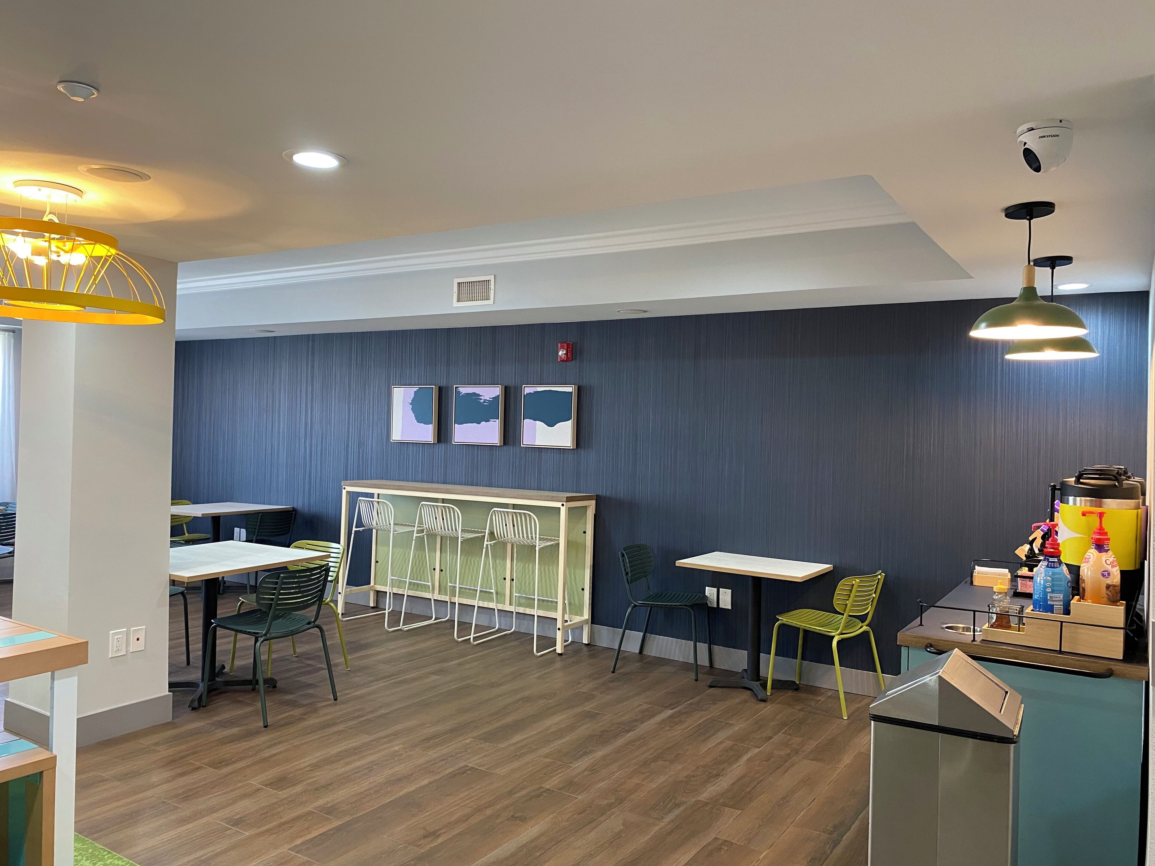 A modern dining area with wooden flooring, a central white table surrounded by chairs, and a yellow pendant light.