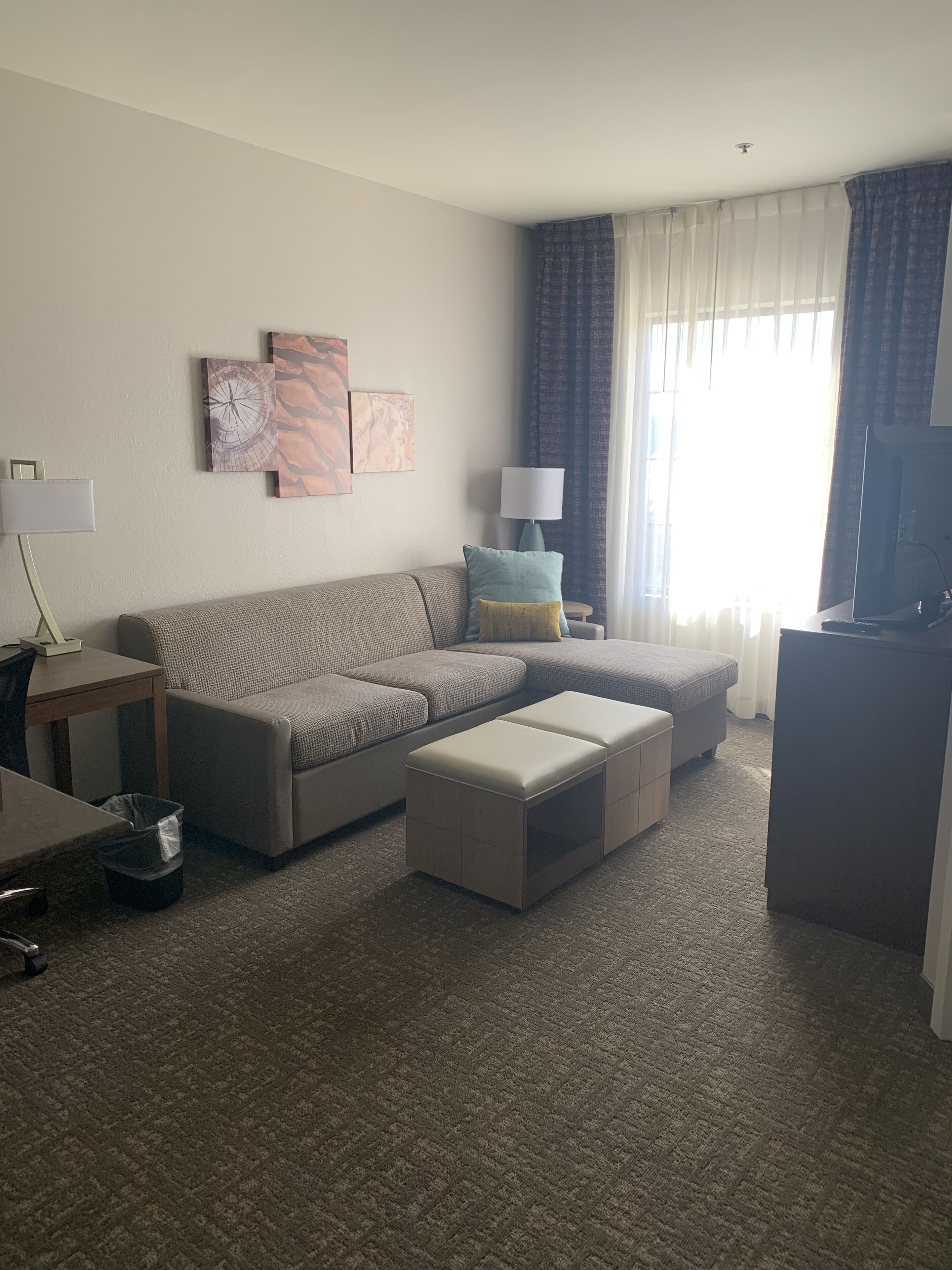 A living room with a sectional sofa, a small table, a lamp, and a television.