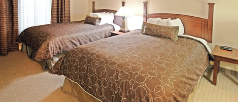 A hotel room with two beds, a nightstand, a lamp, and a remote control on the nightstand.