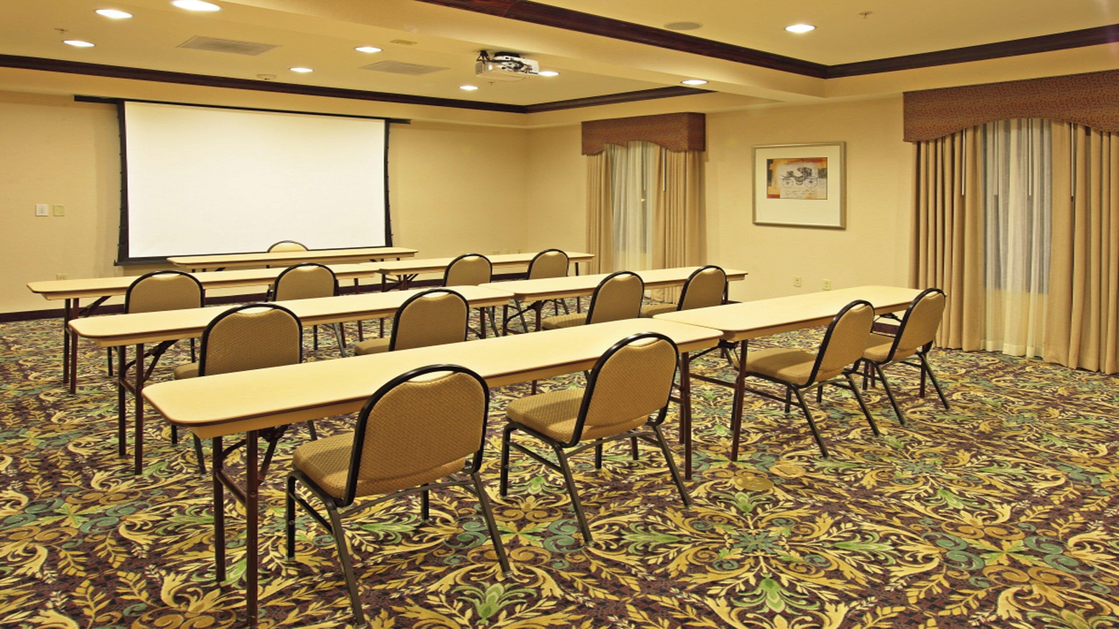 A conference room with long tables and chairs, a projector screen, and a carpeted floor.