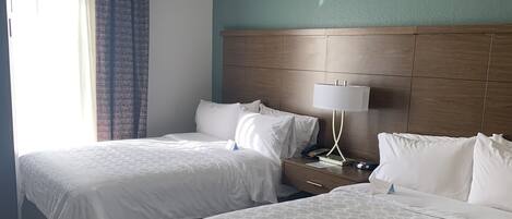 Habitación de hotel con dos camas, cabecera de madera, lámpara de noche y ventana con cortinas.