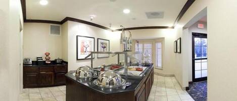A buffet area with a central island, a refrigerator, and a window with blinds.
