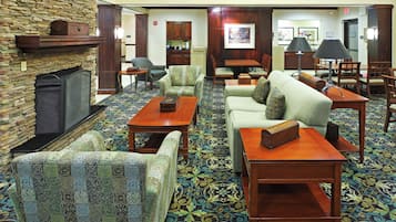 A hotel lobby with patterned carpet, sofas, armchairs, a fireplace, and a dining area.