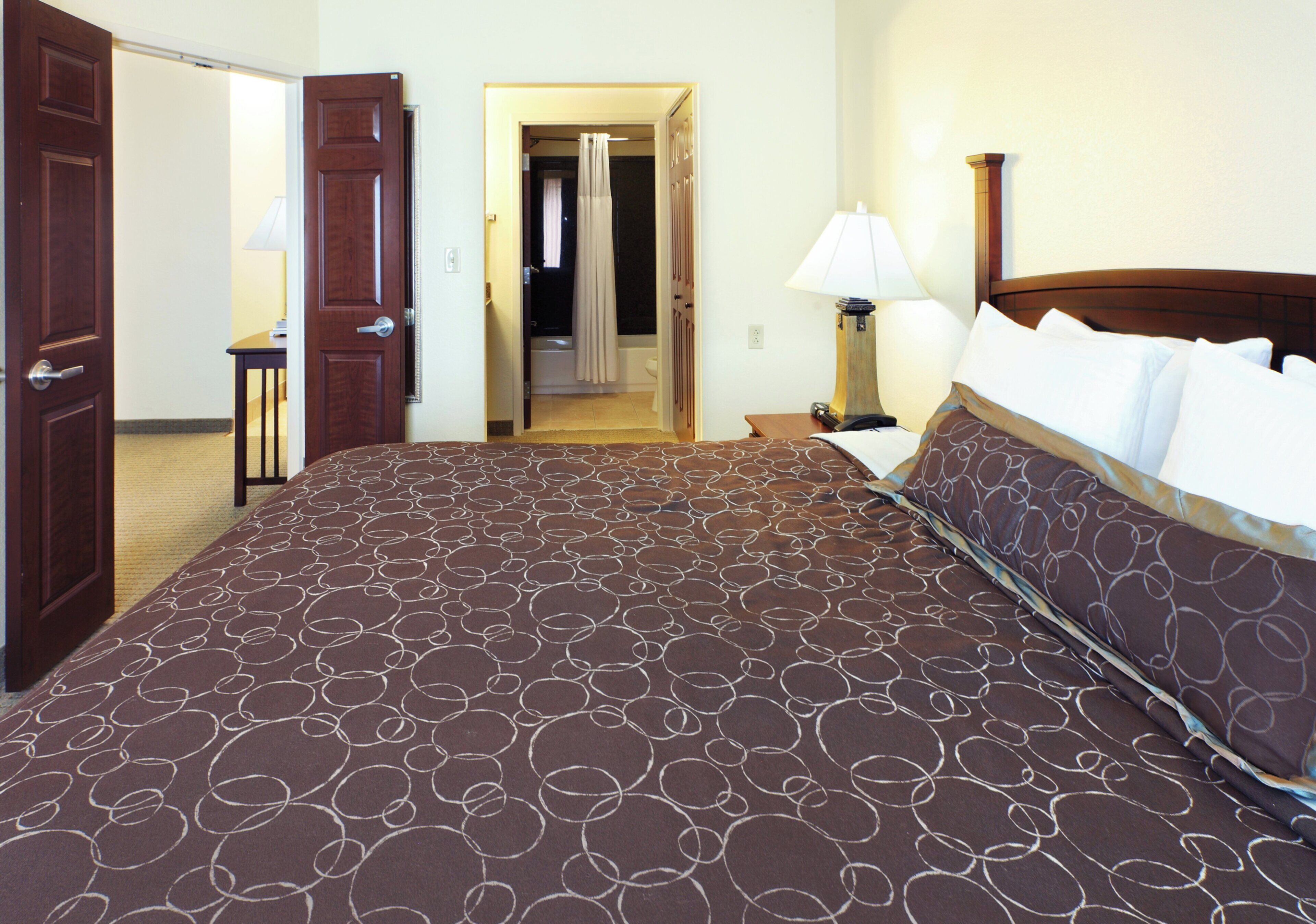 Una habitación de hotel con una cama grande, una mesita de noche, una lámpara y una puerta que da a un baño.
