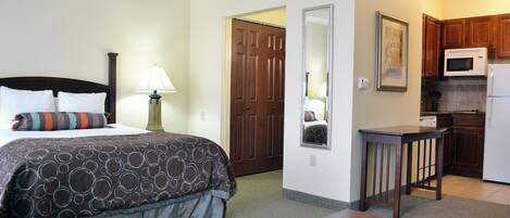 Una habitación de hotel con una cama, mesita de noche, lámpara y una kitchenette equipada con microondas y refrigerador.