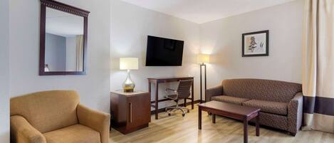 A hotel room with a sofa, armchair, desk, and TV.