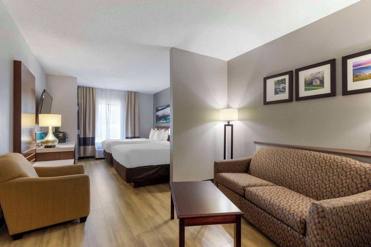 A hotel room with a bed, a sofa, a chair, a desk, and a lamp. There are three framed pictures on the wall.