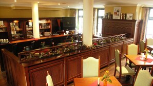 Zona de bar con mobiliario de madera y un televisor. Hay mesas y sillas para comer, y una planta decorativa en la barra.