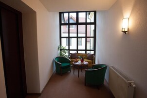 A hallway with a large window, two green armchairs, a small table, and a radiator.