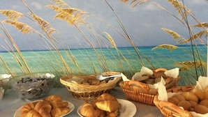 A table with baskets of bread and pastries, set against a backdrop of a beach scene. - Hotel Merano (Grado)