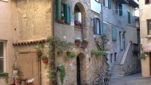 A narrow cobblestone street with a red bicycle parked against a building with stone walls and green shutters. - Hotel Merano (Grado)