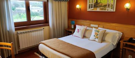A hotel room with a bed, a chair, a nightstand, a wall-mounted lamp, and a window with curtains.