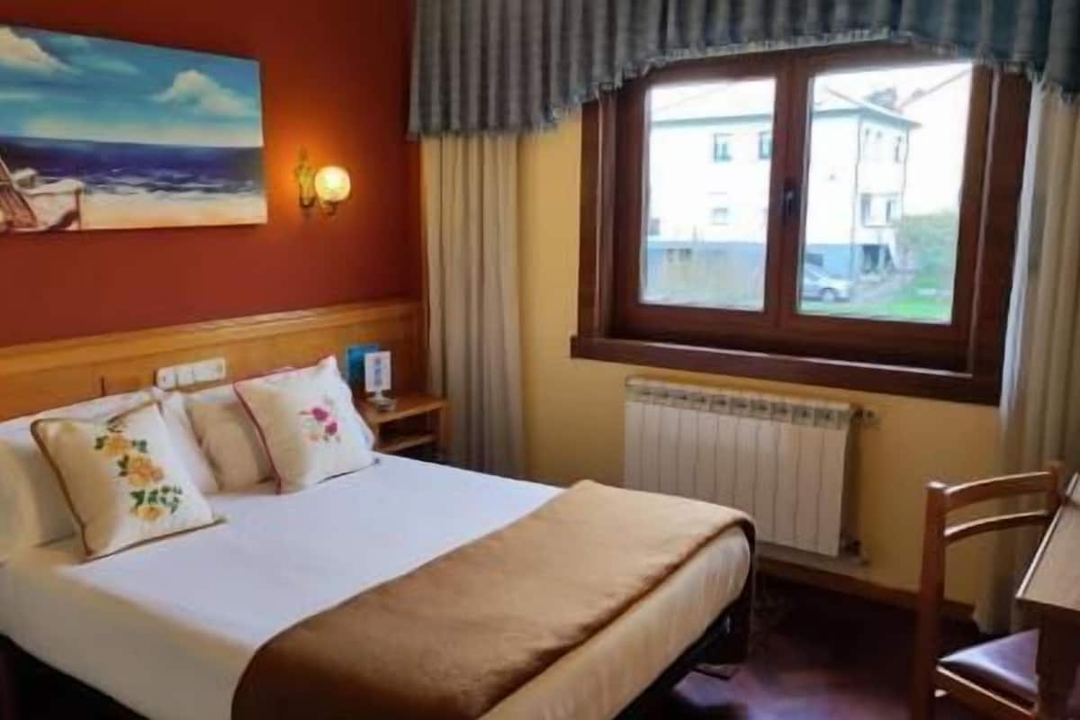 Quarto de hotel com cama, cadeira, mesa, um quadro e janela com vista.