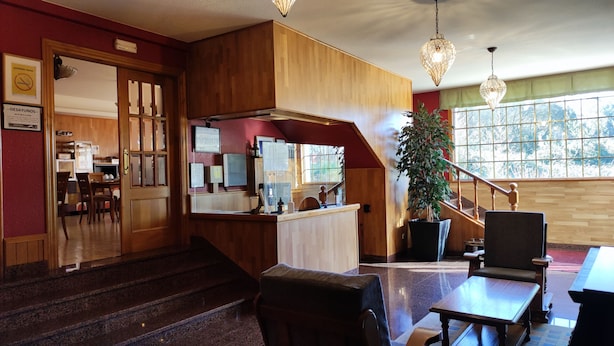 Un hall de hotel con una recepción, una escalera y un amplio ventanal con vistas a árboles.