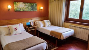 Habitación de hotel con dos camas, cabecera de madera, un cuadro de un bosque, un teléfono y una ventana con cortinas.