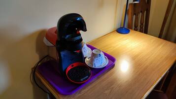 A coffee maker on a purple tray with a wooden table and a chair in the background.