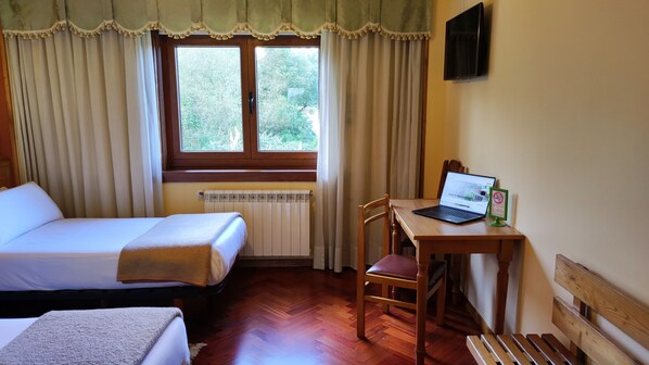 Habitación de hotel con cama, escritorio con computadora portátil, silla, radiador y ventana con cortinas.
