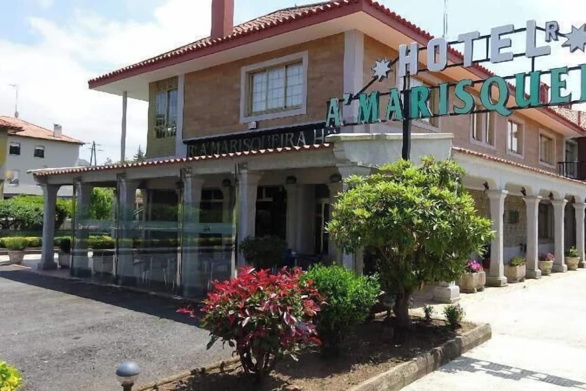 Um hotel chamado 'HOTEL A'MARISQUEIR', com área de estar coberta ao ar livre e uma fileira de vasos de plantas ao longo da calçada.
