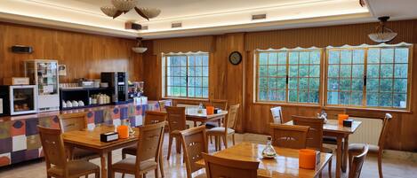 A dining area with wooden tables and chairs, a coffee machine, and a refrigerator.