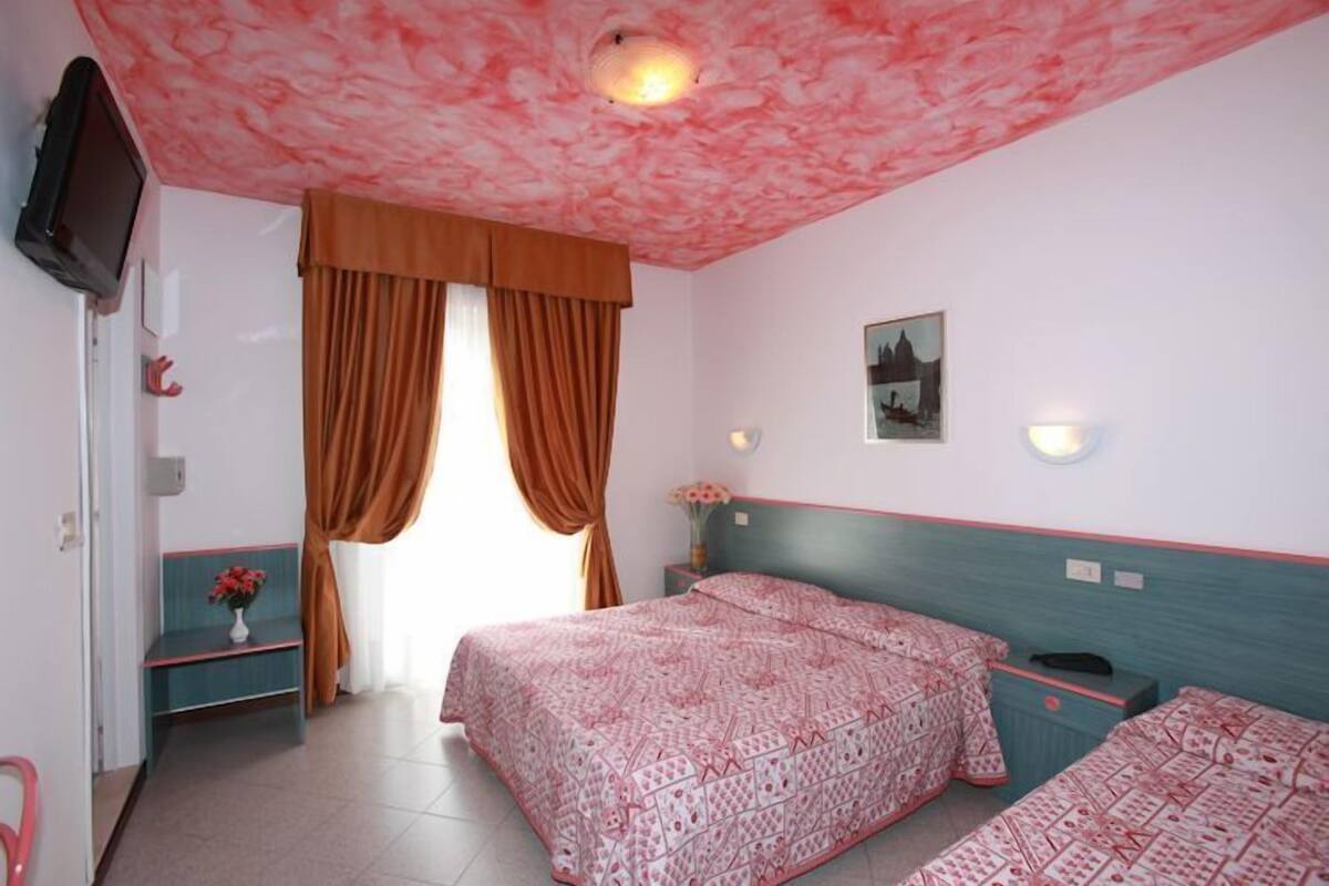 Un dormitorio con dos camas, televisión, ventana con cortinas e imagen colgada en la pared.