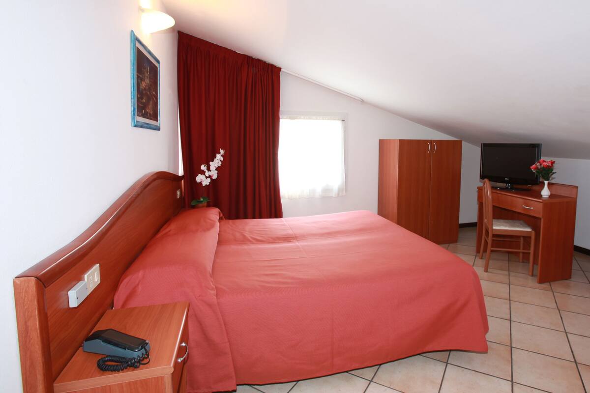 Una habitación de hotel con cama, un escritorio con computadora, televisor y teléfono.
