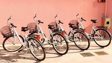 Varias bicicletas estacionadas frente a una pared rosa, cada una con una canasta y un asiento.