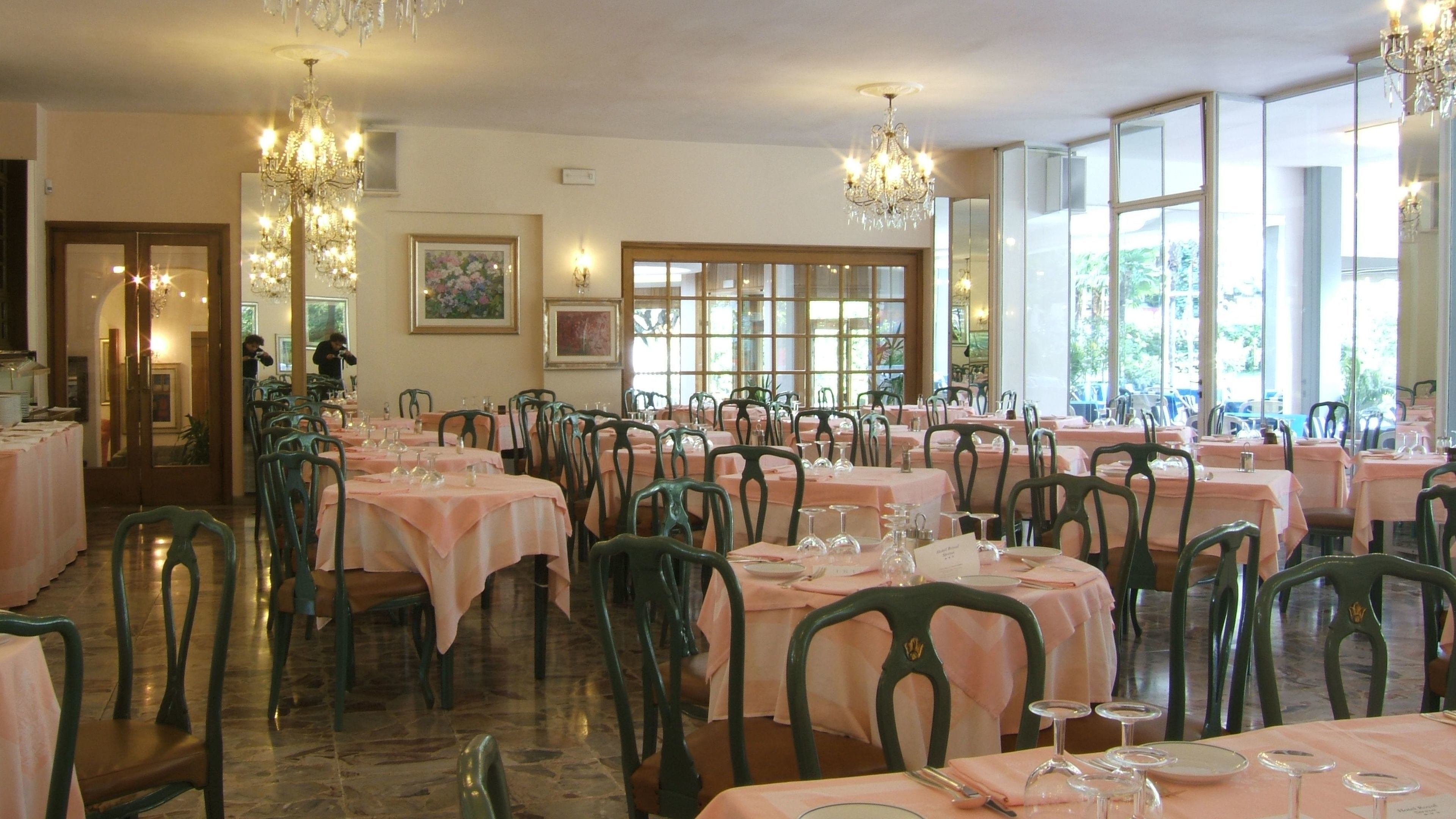 Une salle à manger avec des tables dressées pour le service, de grandes fenêtres et des lustres.
