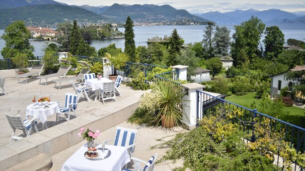 Una terraza al aire libre con mesas y sillas, con vistas a un lago y montañas.