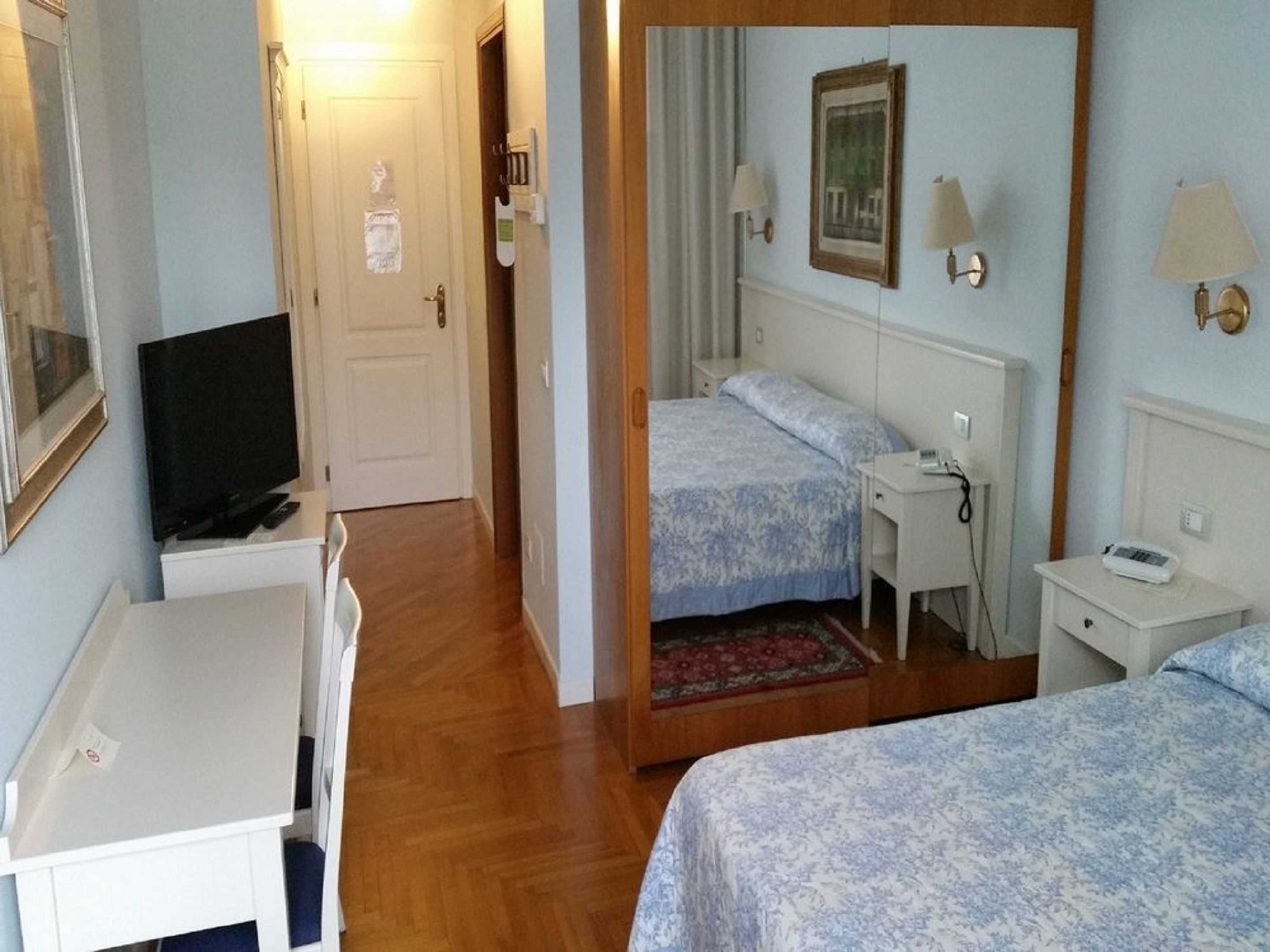 A hotel room with two beds, a desk, a television, and a mirror.