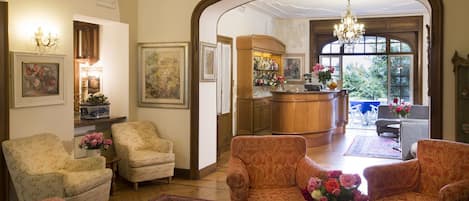 A spacious living room with floral-patterned armchairs, a coffee table with a vase of flowers, and a view into the kitchen through an archway.
