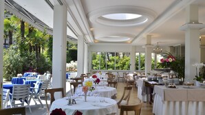 Un amplio comedor interior con mesas redondas, sillas y vistas a la exuberante vegetación exterior.