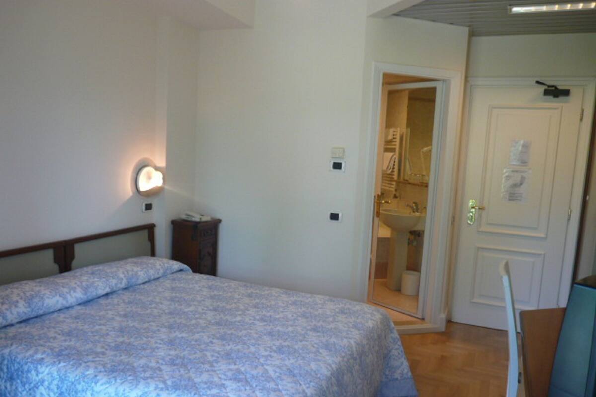 A bedroom with a bed, a bedside table, a lamp, and a door leading to a bathroom.
