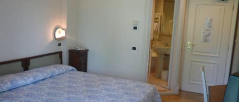 A bedroom with a bed, a bedside table, a lamp, and a door leading to a bathroom.
