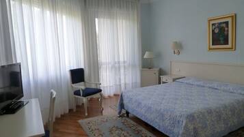 Ein Hotelzimmer mit einem Bett, einem Schreibtisch mit Computer, einem Sessel und einem Bild an der Wand.