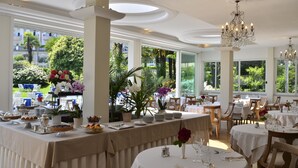 Un restaurante con mesas redondas, manteles blancos y una araña.